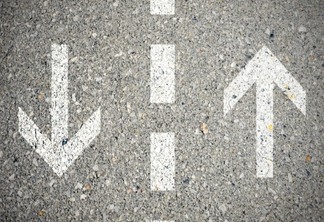 Imagem em close de marcações no asfalto numa via de duas mãos, com uma seta para cima e outra para baixo.