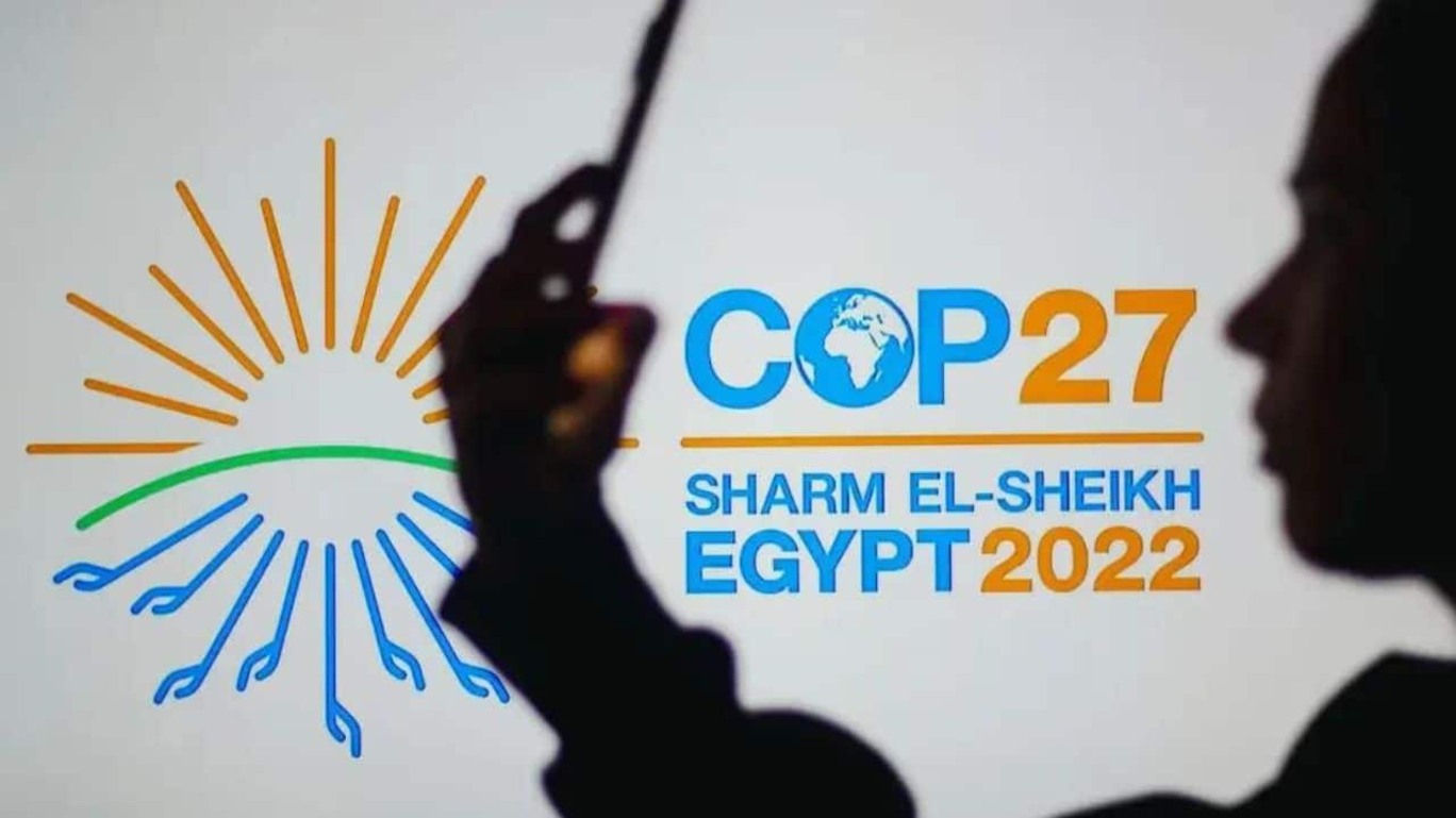 Logomarca da COP27 ao fundo com perfil da uma pessoa em primeiro plano