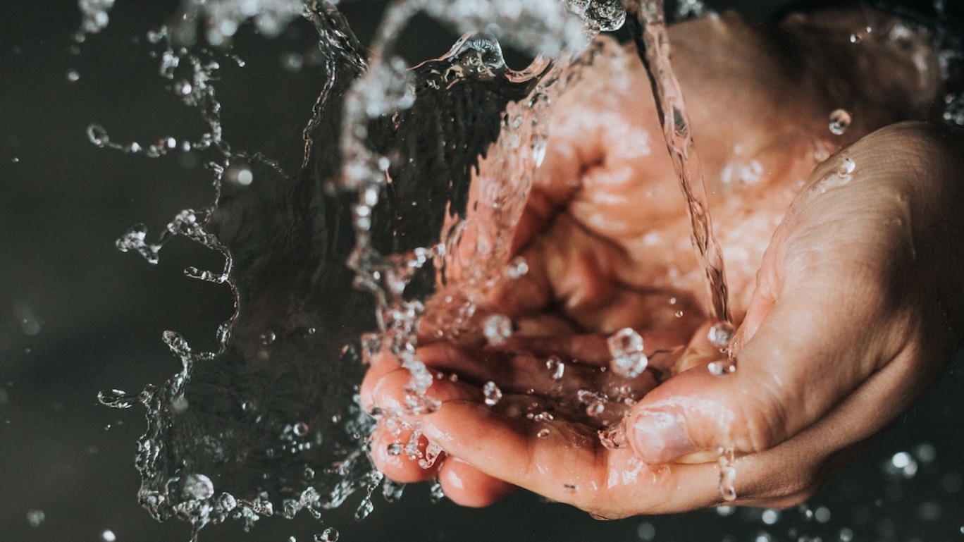 Foto mostra mãos sendo banhadas por água limpa