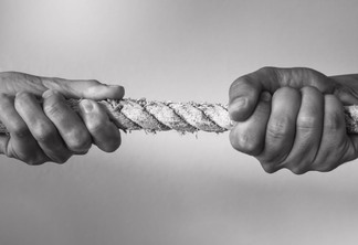 imagem em preto e branco mostra uma corda esticada sendo puxada para lados opostos por duas mãos