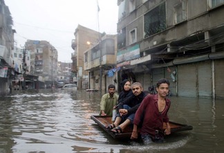 Quatro pessoas andam por uma rua tomada pela enchente no Paquistão.