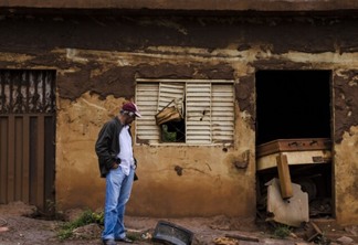 Homem olha para destroços de casa atolada pela lama após o rompimento da barragem do Fundão, em Mariana