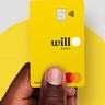 A mão de uma pessoa negra segura um cartão amarelo do Will Bank