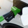 Uma bomba de combustível na cor verde, com os dizeres "bio", abastecendo um carro branco